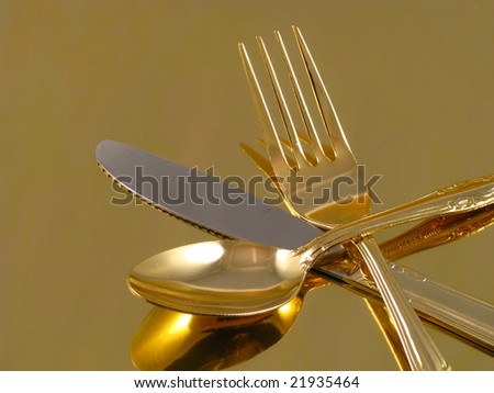 Shiny Gold Dinnerware Fork, Knife, and Spoon Arranged and Isolated on a Reflective Gold Background as an Abstract Closeup