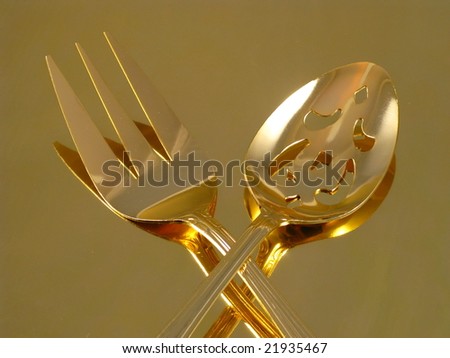 Shiny Gold Flatware Serving Spoon and Fork Arranged and Isolated on a Reflective Gold Background as an Abstract Closeup
