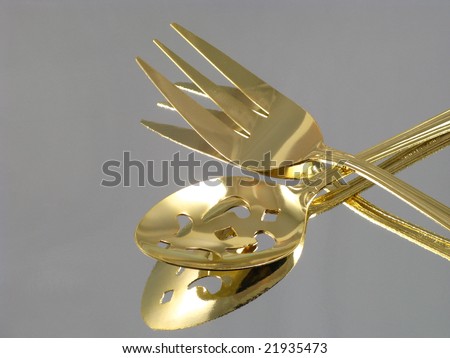 Shiny Gold Dining Serving Spoon and Fork Arranged and Isolated on a Reflective Silver Background as an Abstract Closeup