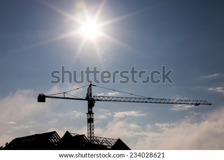 Silhouettes of tower crane at construction side, over sun at sunrise, cloud with blue sky of background