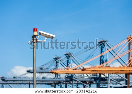 CCTV cameras with warning lights on steel pole and blurred crane in port background