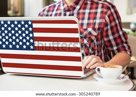 Man sitting in a cafe with cup of coffee and notebook with American flag on it. English language learning concept