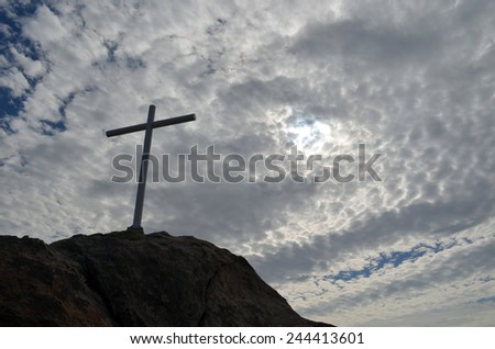Hope.  If we look up in the sky and see nothing but clouds we sometimes have to rely on our faith.  Cross on a small rock with a cloudy sky in the background.