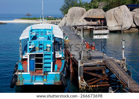 A wooden blue diving boat on the jetty of Nang Yuan Island Resort with the white sand beach on the background and a part of island.