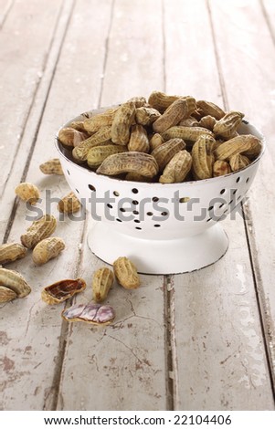 boiled peanut in a white retro bowl, some are dropped on wood ground.