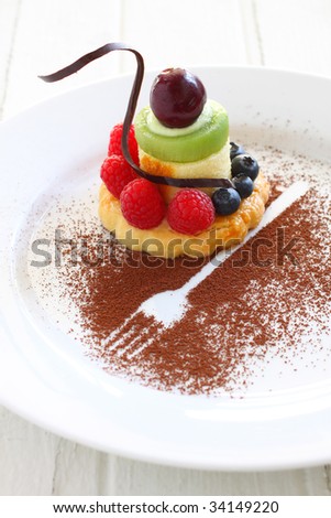 fruit tart with fresh fruit like kiwi, blueberry, raspberry, cherry, styling with chocolate piece and cocoa powder .