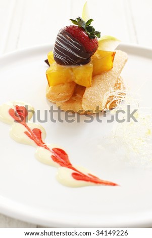 fruit tart with fresh fruit like starfruit,  styling with chocolate coated strawberry, biscuit vanilla sauce .