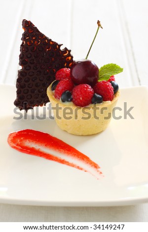 fruit tart with fresh fruit like kiwi, blueberry, rassberry cherry, styling with chocolate comb and strawberry sauce and mint leave.
