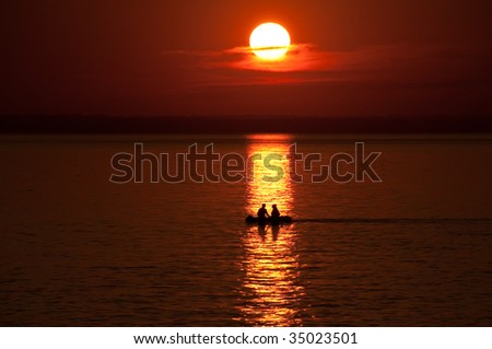Boat with 2 people against an orange sunset