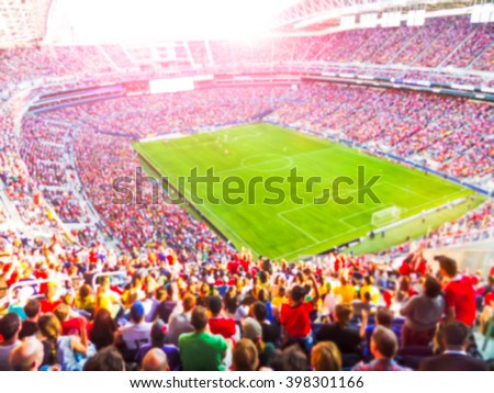 Football- soccer fans cheer their team and celebrate goal in full stadium with open air  with bright lighting beam     -blurred picture.