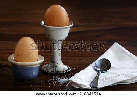 Breakfast, two eggs in egg cups, spoon and napkin on a dark brown table