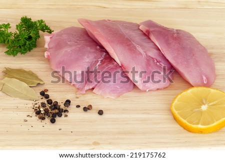 three pieces of raw meat on a wooden board, turkey steak with spices before cooking