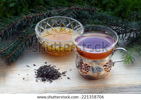 black tea and honey in nostalgic glasses and some loose tea on an old wooden board, fir tree in the background, suitable for autumn, winter and christmas, horizontal