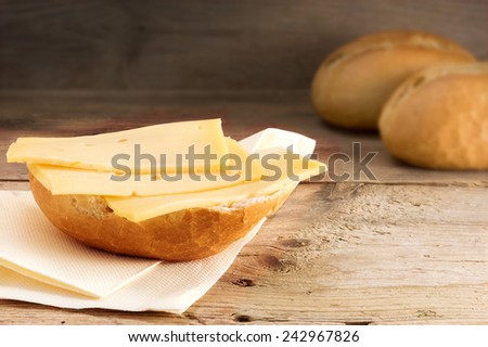 half a bun with cheese and blurry bread rolls in the background on old wood