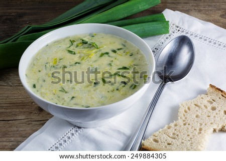 leek cream soup in a white bowl with spoon, napkin and fresh leek od rustic wood