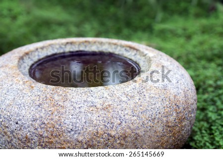 round water basin or bird bath of natural stone granite on ground cover plants, puristic garden scene, zen style