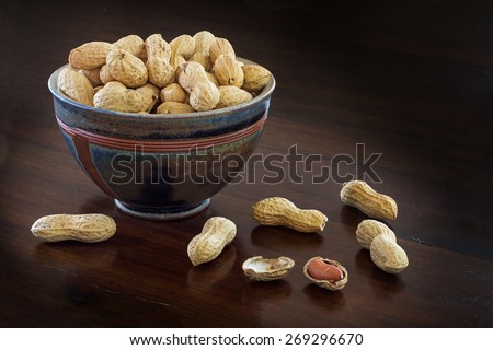 peanuts in shells  in a handmade ceramic bowl on a  brown table, copy space in the dark background