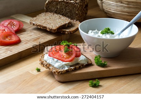 fresh curd cheese dip with herbs in a white bowl and rustic wholegrain bread with tomatoes on a kitchen board, healthy and powerful meal with natural food products