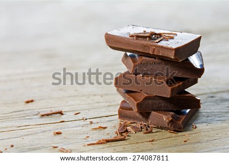 stack of chocolate pieces, close up shot with selected focus on a bright rustic wooden background
