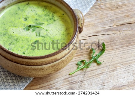green vegetable soup with broccoli, rucola and spinach in a brown  bowl on a rustic wooden board