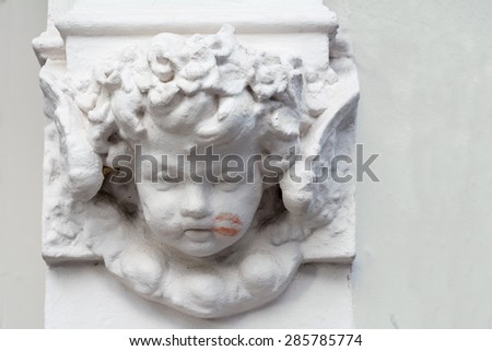 cherub as decoration on a building with a lipstick kiss on his cheek, copy space in the blurred background