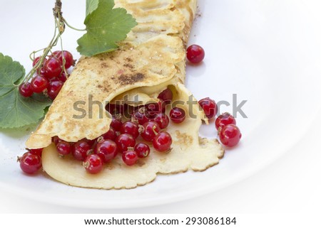 wrapped pancake or crepe with fresh red currants on a white plate as a summer dessert, copy space