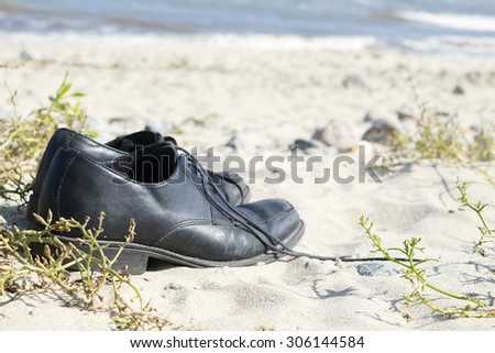 black men\'s shoes standing on the sandy beach, vacation background with narrow depth of field