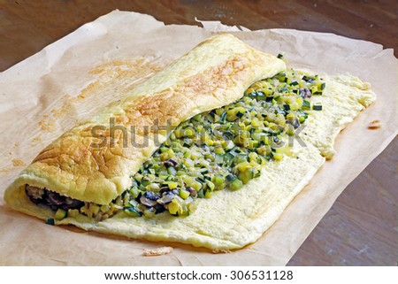 omelet plate with zucchini and vegetable filling on baking parchment to make a roll