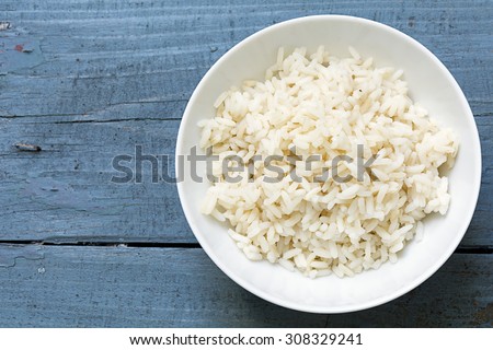 Boiled rice in a white china bowl on a rustic blue wooden table, copy space in the background