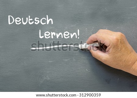 Hand on a chalkboard with the German words Deutsch lernen (Learning German). Language class concept showing teacher hand writing on the blackboard.