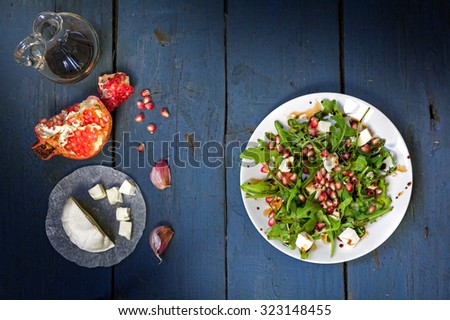preparing salad with arugula, feta cheese, pomegranate, garlic and balsamic dressing served on a white plate on an old blue wooden table, view from above