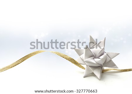 White paper star for Christmas decoration, also called Froebel or German star, with golden ribbon on a light blue background fading to white