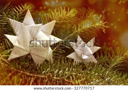 two paper stars, also called Froebel or German star, in a fir branch, shimmering red golden christmas light bokeh in the background