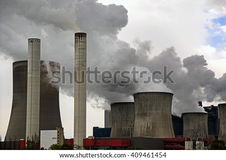power plant with chimneys and steaming cooling towers, gray clouds rise in the sky, concept for energy industry, co2 emissions and environmental protection