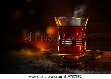 Cup of Turkish tea on saucer on rustic wood with snow in front of a dark blurred background with red and golden bokeh lights, copy space, selected focus, narrow depth of field