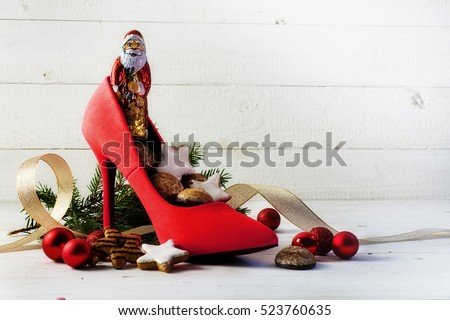 ladies red high heel shoe filled with sweets and christmas decoration for Nicholas day on the 6th December in Germany, white rustic wooden background with copy space, selective focus