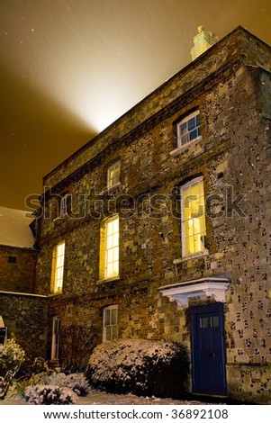 Winter in England - a medieval stone house at night during snowing warmly lit by streetlamps
