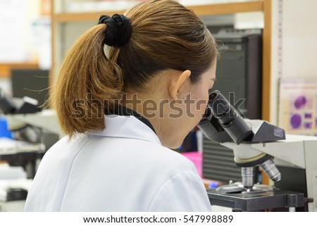 Women scientist looking to microscope eyepiece in clinical laboratory.