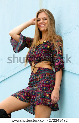 Beautiful young woman smiling and wearing a fashion dress and leaning against blue wall