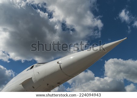 Pointed nose cone and windscreen of the supersonic aircraft Concorde against a blue sky with white clouds, shot from beneath