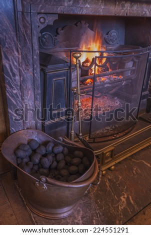 Roaring open fire in a country house setting with a marble fireplace and coal scuttle.