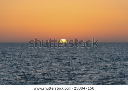 The sun disappearing over the horizon at sunset with the sea in the foreground