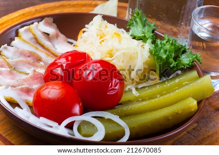Assorted pickles and pickled vegetables with bacon slices, served on a wooden plate.
