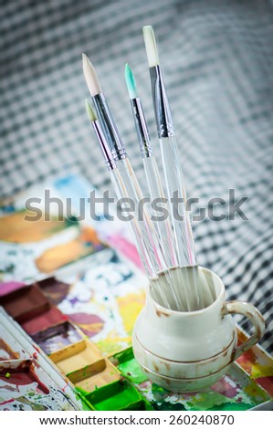 Art paint brushes in cup with colorful palette