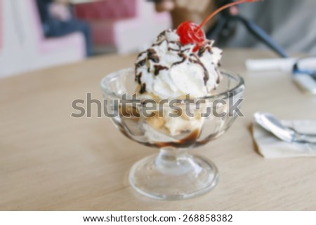 blurry Vanilla sundae ice cream with sauce, wafer, sweet cherry, mint and chocolate curls in cup on table