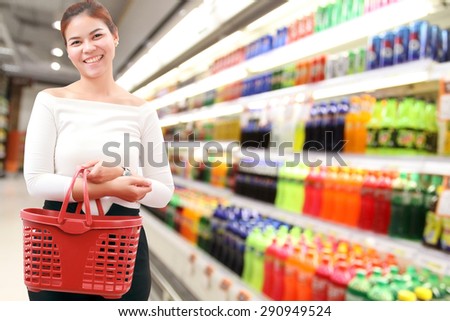 happiness, consumerism, sale and people concept - smiling young woman Asian with shopping basket and buy coca-cola and sparkling water at supermarket/mall