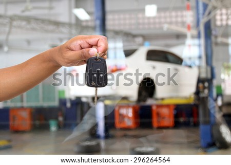 close up of hand holding keys on cars on lifts in small service station for background