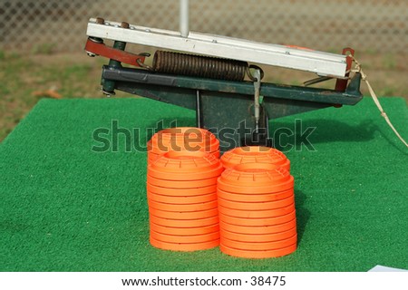 Clay pigeons stacked next to a portable trap thrower mounted on a table at a trap and skeet club