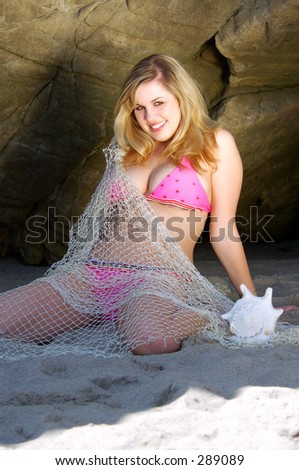 Pretty blond bikini model washed up on shore in a fish net with conch shell.