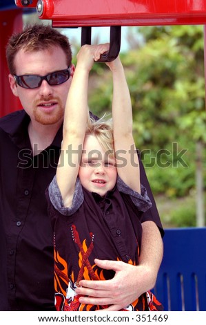 Blond boy child in a rock and roll flame shirt and father playing together at the park